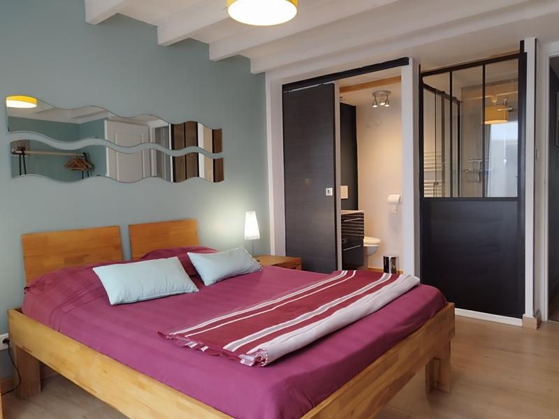 Une chambre avec un lit double, vue sur la salle d'eau avec lavabo et toilette.