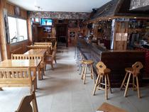 Salle d'accueil du restaurant, comptoir bar en bois laqué, tables et chaises, tabourets, salle de jeux au fond, TV, fenêtres donnant sur l'extérieur
