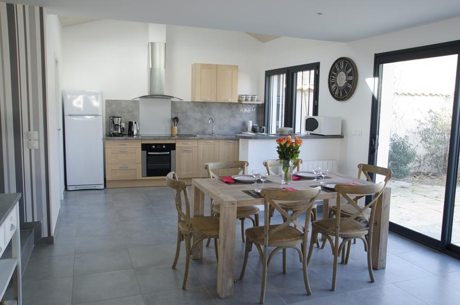 Une table dressée avec chaises, dans le fobnd l'espace cuisine ouverte tout équipée.