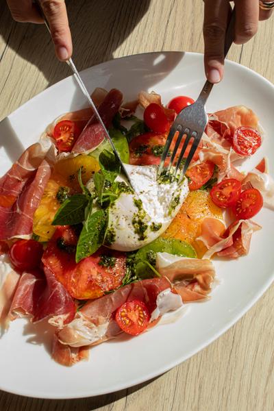 Une assiette avec une burrata, de la charcuterie, des tomates.