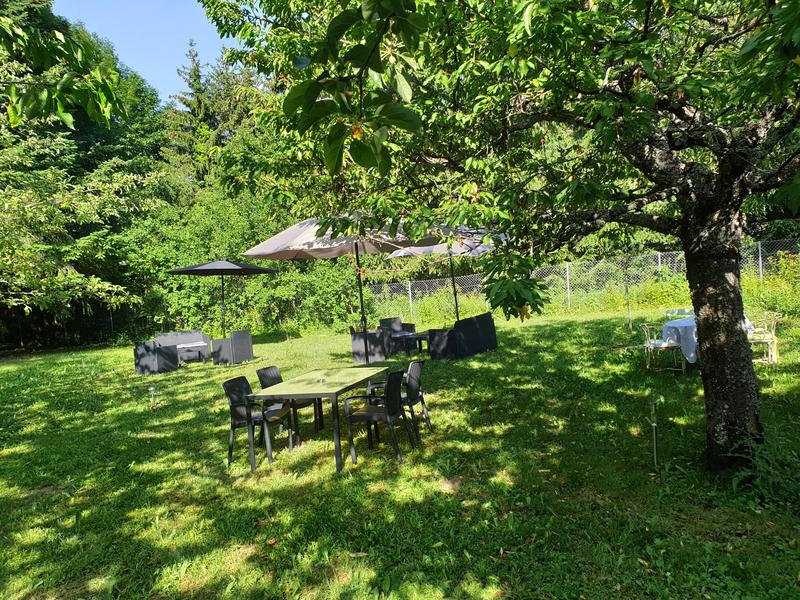 Une table et deux salons de détente installés dans un écrin végétal, ombragés par des parasols