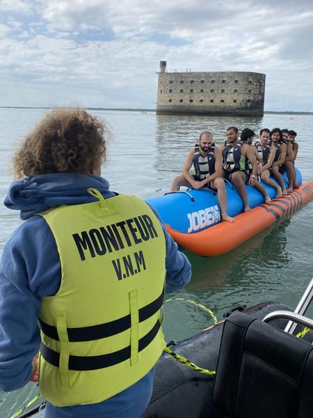 Le moniteur de dos, un groupe d'hommes de face sur une bouée tractée banane, en fond le Fort Boyard.