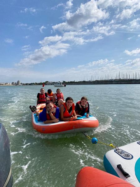 6 personnes assises et allongées sur un paddle géant tracté pour sortir du port.