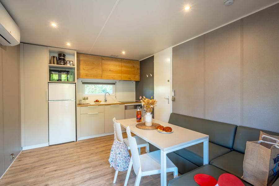 L'espace vie d'un mobile home, avec la cuisine ouverte, deux chaises, une table et une grande banquette d'angle.