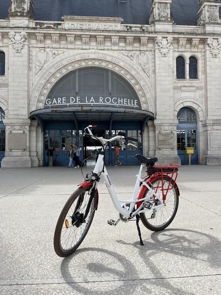 Un vélo blanc et rouge sur le parvis devant l'entrée de la gare.