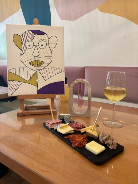 Une table avec une planche de charcuterie et fromage, et un tableau sur un chevalet