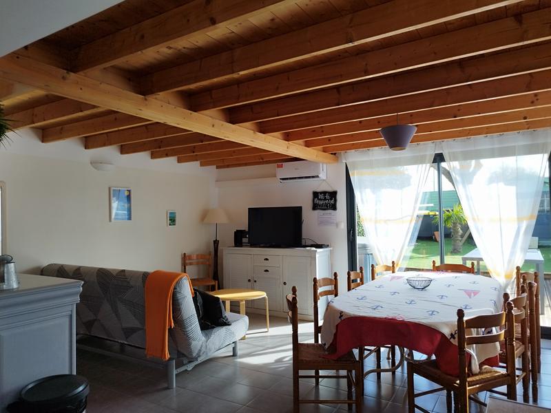 Un salon séjour avec canapé, télévision posée sur un meuble, table à manger,. Porte fenêtre avec vue sur l'extérieur.