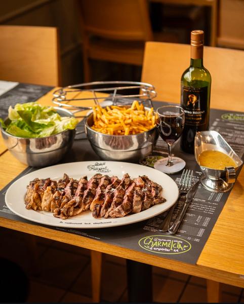 Une entrecôte découpée servie avec des frites, de la salade et du vin rouge.