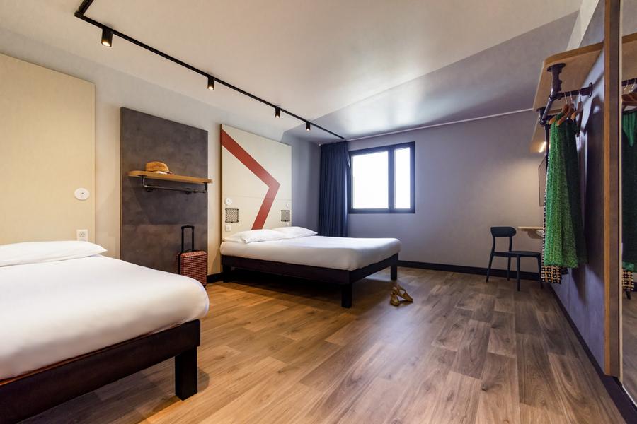 Une chambre avec deux lits doubles, un portant avec quelques vêtements.