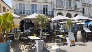 La terrasse vide du restaurant, avec des tables, chaises, parasols, plantes.