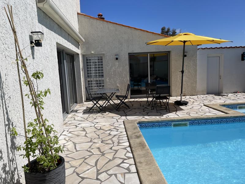 La terrasse avec piscine découverte, un salon de jardin métallique et un parasol sur pied.