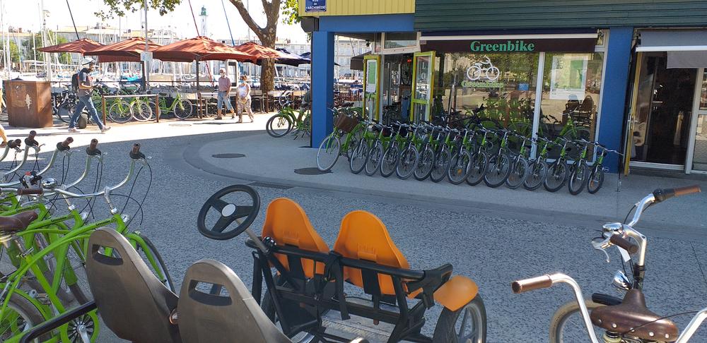 Une vingtaine de vélos verts et une rosalie, devant l'entrée de la boutique et sur le tottoir en face.