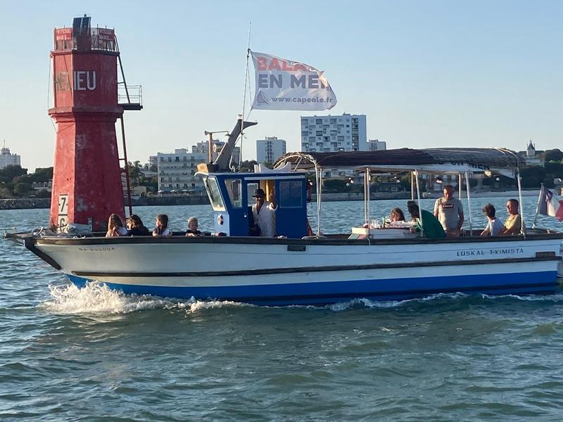Un bateau à moteur avec passagers sortant du port, au niveau de la balise rouge.