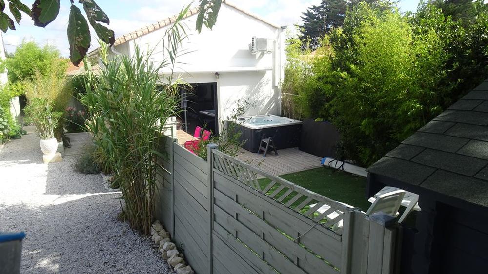 Vue sur la terrasse avec jaccuzzi et sur le parking privé, séparé par une palissade en bois.