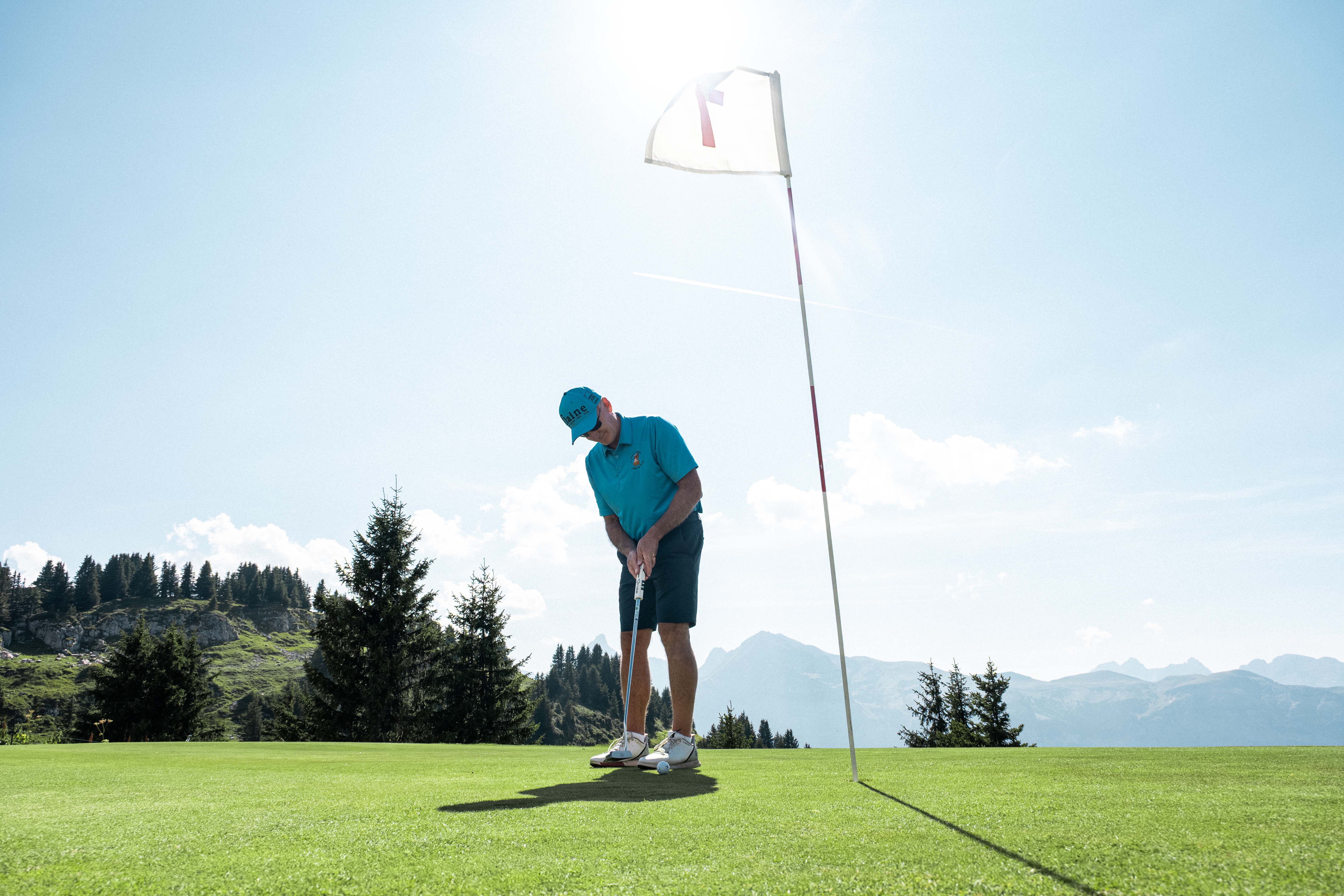 Un homme joue au golf sur un green en montagne