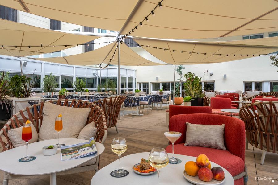 La terrasse ombragée par des grandes toiles, avec bon nombre de tables et de fauteuils.