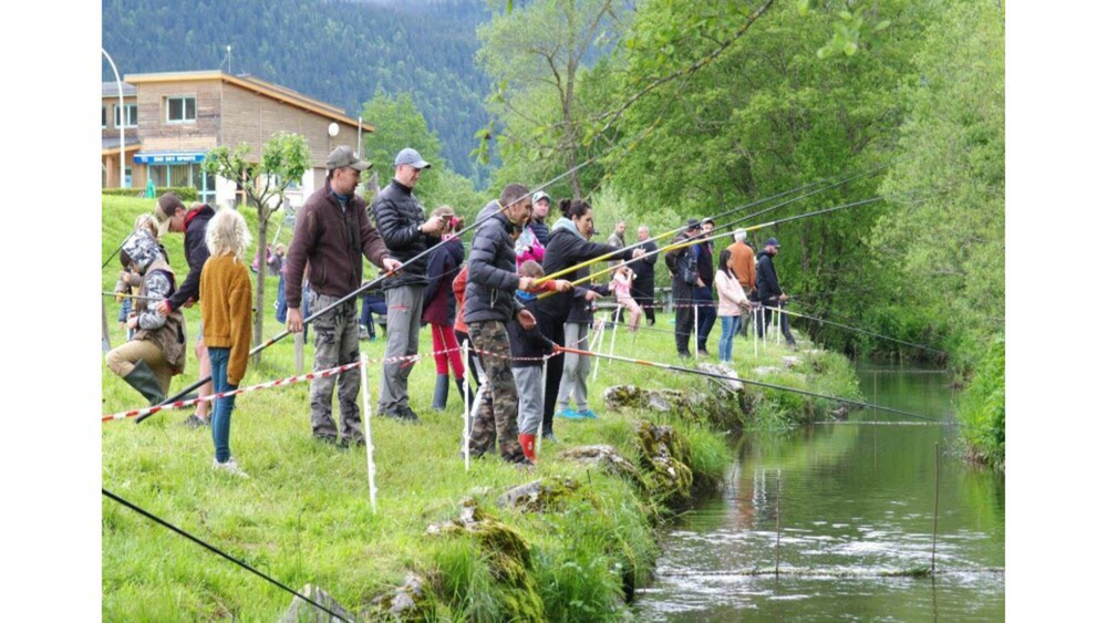 Des enfants comme des adultes sont au bord d'une rivière avec de grandes canne-à-pêche.