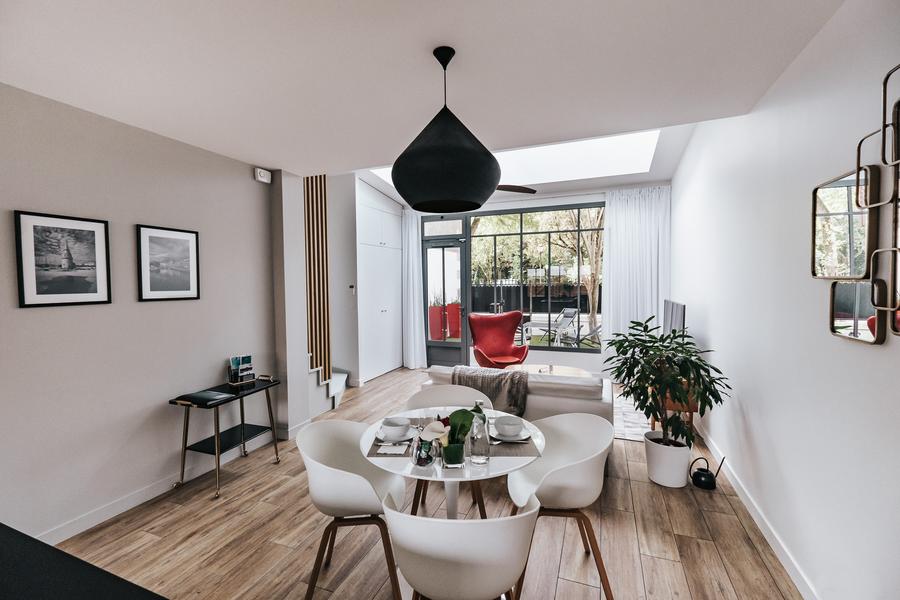 En enfilade le séjour avec table et chaises, le salon avec canapé et fauteuil, au fond une grande baie et porte vitrée donnant sur le jardin.