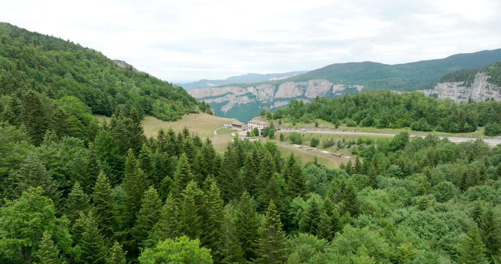 En contre plongée l’établissement se dévoile au loin entre les arbres et entouré de verdure avec en toile de fond les montagnes