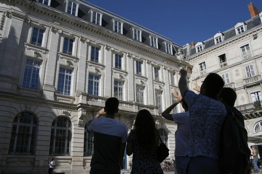 Un groupe de personne devant le bâtiment un vieux bâtiment, sur la place de l'Hôtel de ville.
