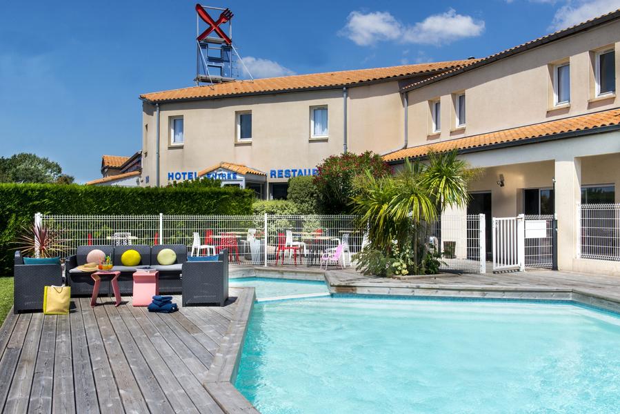 Une piscine extérieure, au fond l'hôtel.