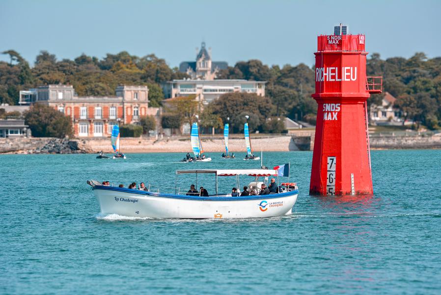 La chaloupe avec une dizaine de personnes à bord, en mer passant à côté d'une balise rouge.