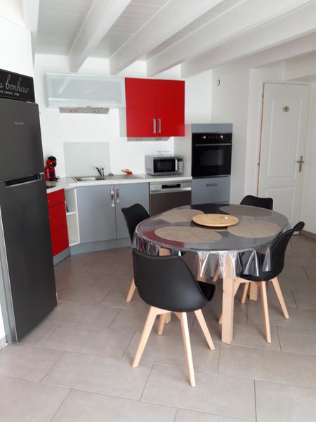 Cuisine ouverte tout équipée, frigo, une table et quatre chaises.