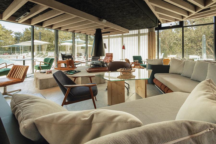 Une partie commune de l'hôtel avec des canapés, des fauteuils et des tables, avec vue sur la pisicne extérieure.