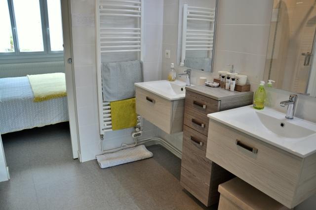 Une salle d'eau avec double basque, sèche serviette, donnant sur une chambre.
