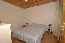 Chambre à coucher sous combles avec lit double, ameublement bois, carrelage