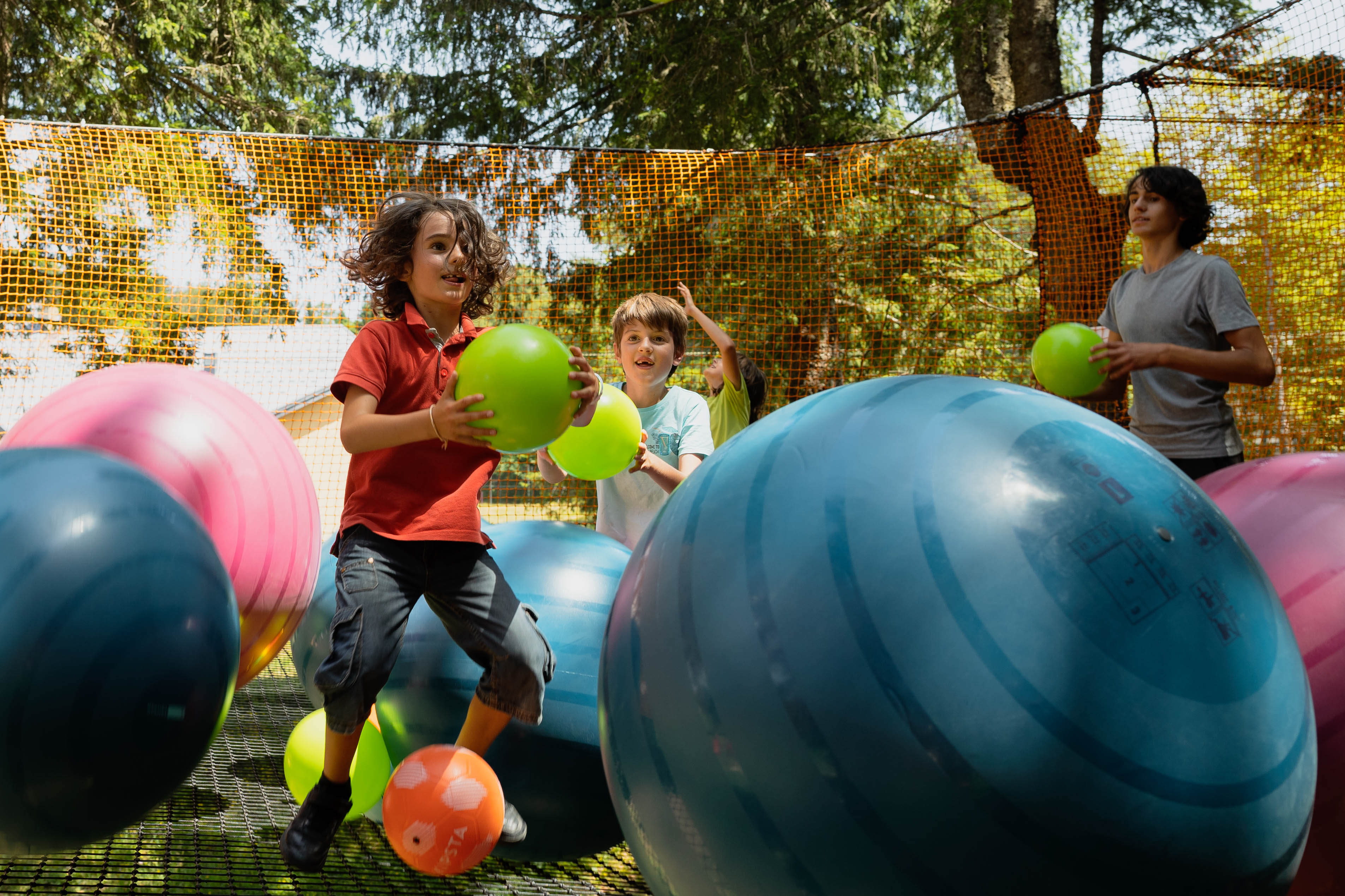 3 enfants, avec un ballon dans les mains, jouent au milieu de gros ballons.