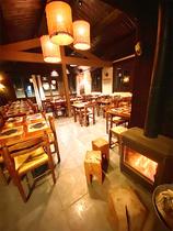 Salle intérieure du restaurant, ambiance confortable avec tables et chaises en bois, sol carrelé, poêle à bois