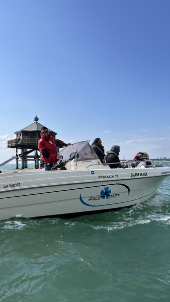 Un bateau à moteur avec des clients et le skipper devant le phare du Bout du Monde.