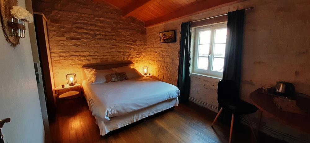 Une chambre avec un lit double, le mur est en pierre blanche, la pièce éclairée par les lampes de chevet.