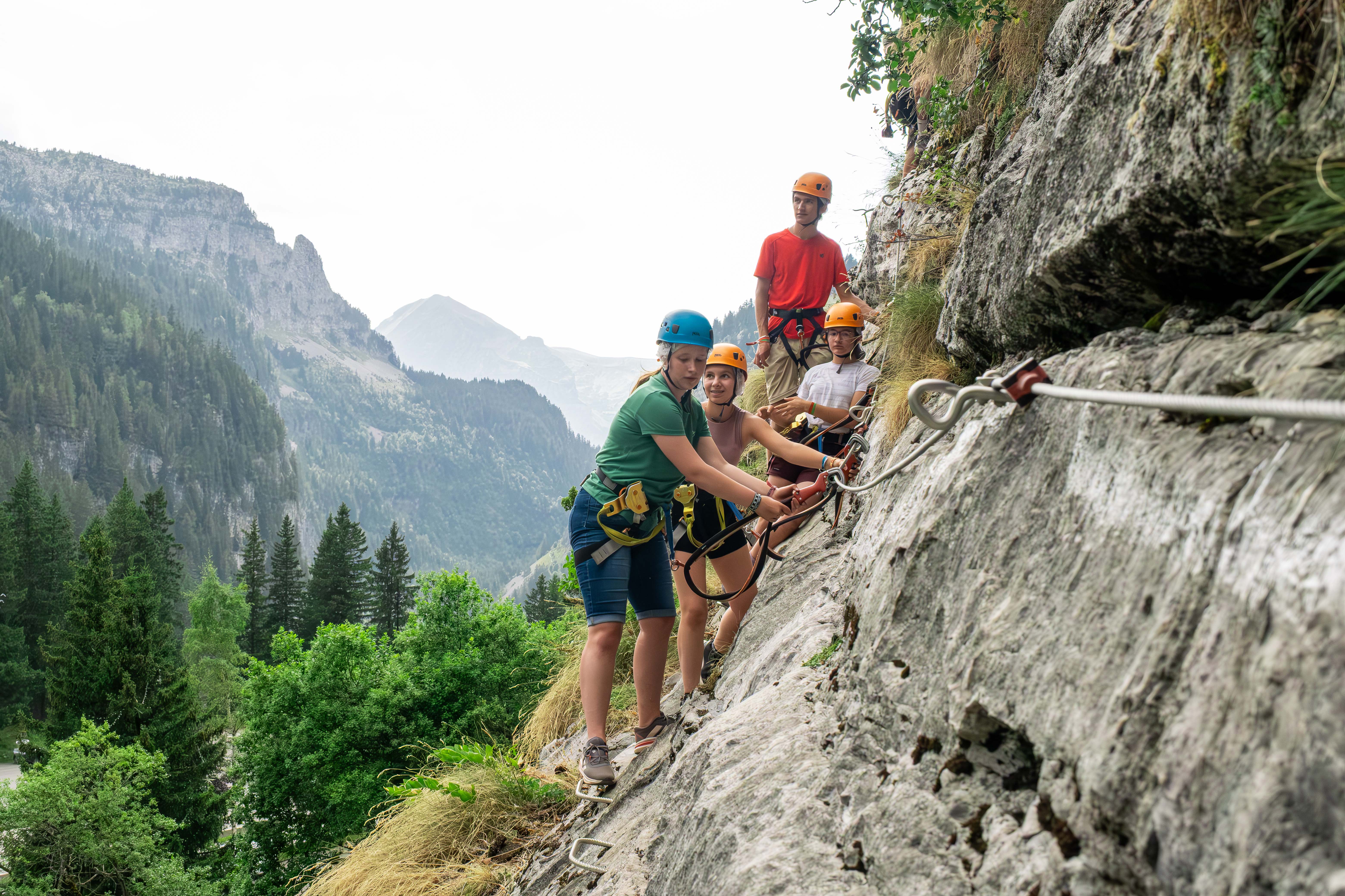Des jeunes s'engagent sur une via ferrata en montagne.