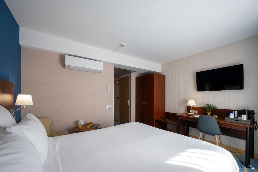 Une chambre avec lit double, climatiseur, télévision accrochée au mur, un bureau, une chaise.