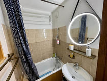 Vue d'ensemble de la salle de bain avec baignoire-douche et son rideau, lavabo et miroir