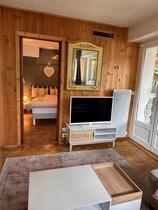 Salon lumineux de chalet tout confort avec table basse, TV, porte vers la chambre à coucher