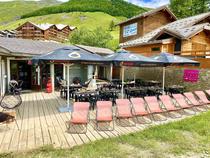 Terrasse de l'établissement en été, tables, chaises, parasols, chaises longues, au milieu de la station et de végétation