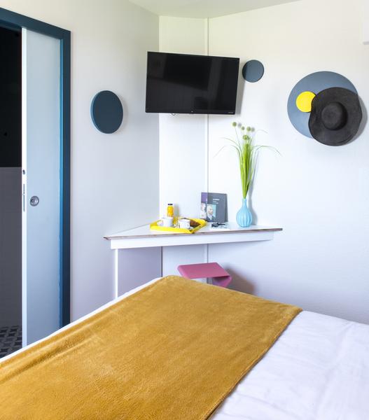 Un coin de lit et une télévision accrochée au mur.