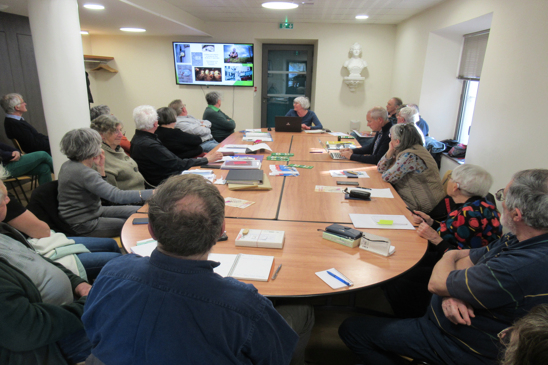 Autour d'une table de réunion sont assis des adultes (membres de l'association GPV). Ils sont tous de dos et regardent un écran.