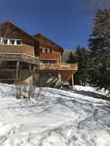 Vue extérieure du chalet en bois et pierre sur 3 étages, avec terrasse en bois