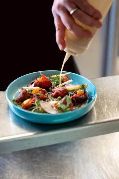 une personne versant de la sauce sur une salade composée.