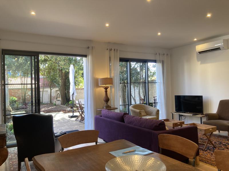 Salon séjour avec vue sur la terrasse et le jardin. Table à manger, chaises, fauteuils, canapé, télévision.