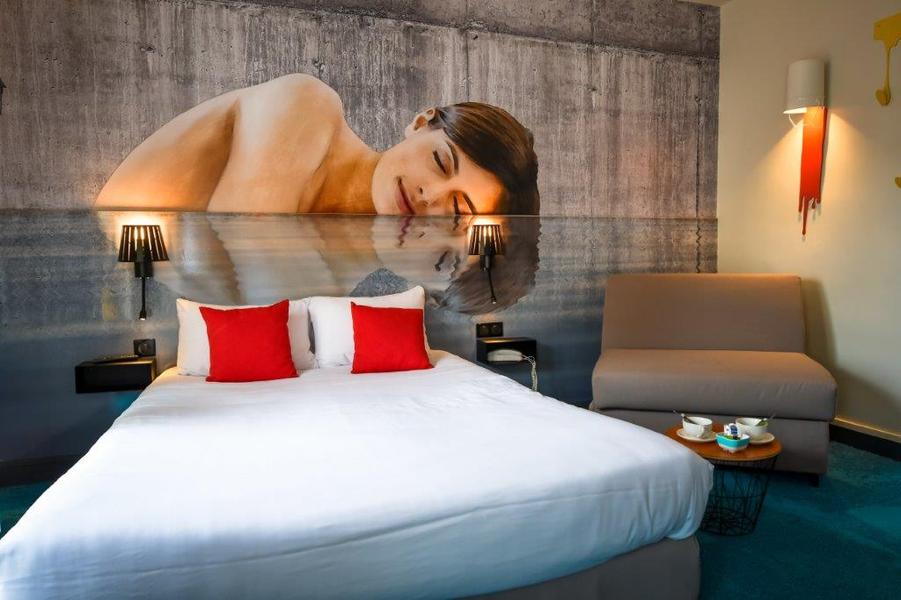 Une chambre avec lit double, Une peinture du visage et haut du corps d'une femme au mur.
