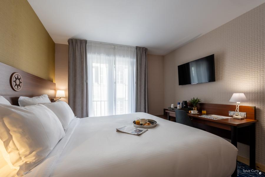 Une chambre avec lit double, télévision accrochée au mur, un bureau, une chaise.
