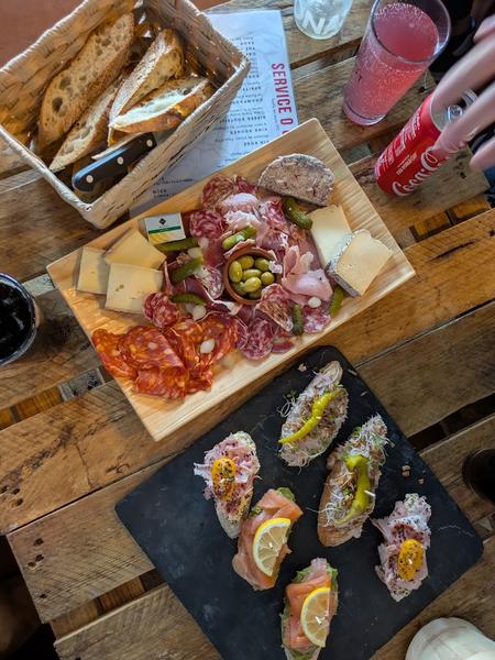 Une ardoise avec des tartines garnies, une plancheb de charcuterie et fromages, une panière de pain.