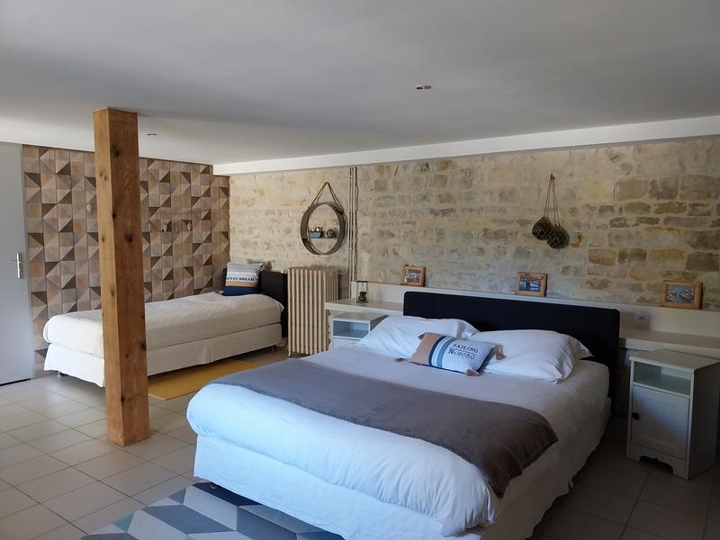 Une chambre avec un lit double et un lit simple, le mur est en vieilles pierres.