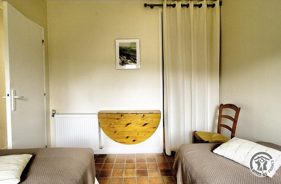 Gîte - 4 personnes - La Voisinée à Chenelette en Haut Beaujolais à proximité du Col des Echarmeaux dans le Rhône : la chambre avec 2 lits simples (rez-de-chaussée), petite table et placard mural.