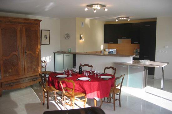 Vue sur la salle à manger avec une table dressée pour 6 personnes, en fond le coin cuisine